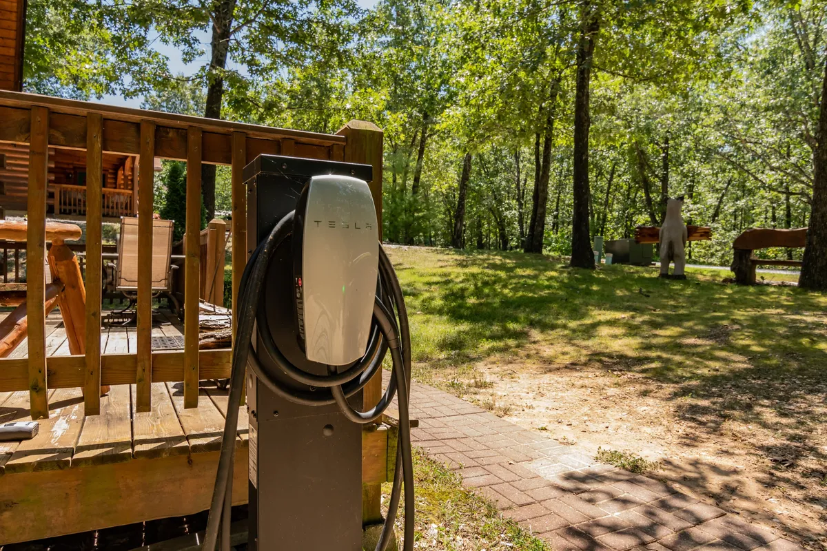 An exterior image highlighting the on-site Tesla/electric car charging station set amid lush greenery, with a wooden deck nearby for outdoor relaxation.
