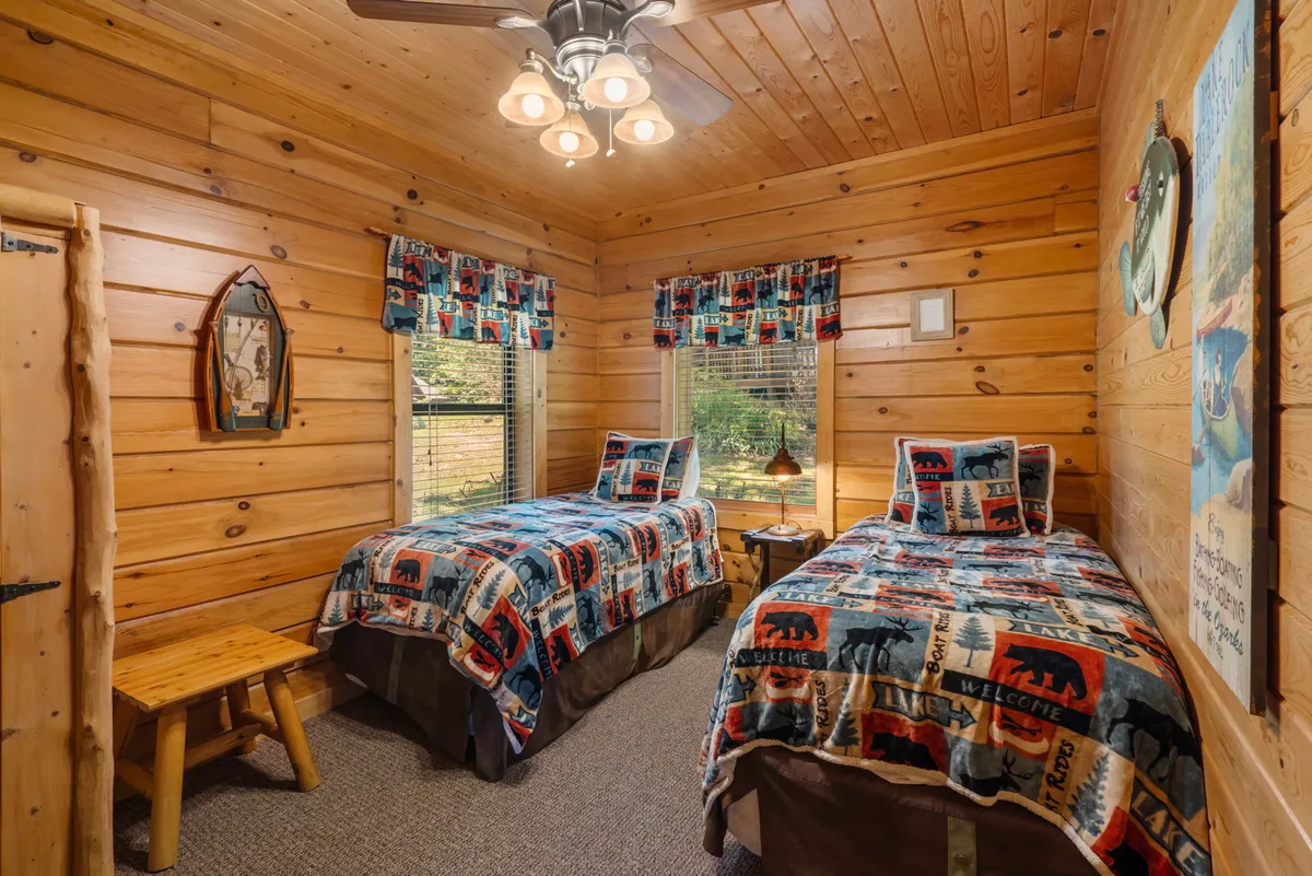 A bright and homey bedroom with two twin beds, each adorned with patterned quilts, a wooden bench at the foot, and attractive framed wall art. The room exudes a welcoming and comfortable vibe for families or groups.