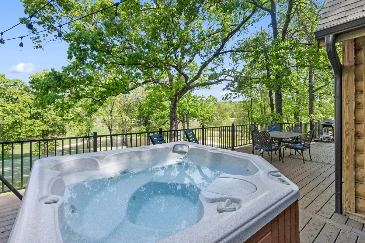 An inviting outdoor deck featuring a sparkling hot tub surrounded by lush greenery and an outdoor dining set. The arrangement is ideal for both relaxation and socializing, with ample space to enjoy meals or unwind in the hot tub while taking in sunset views.