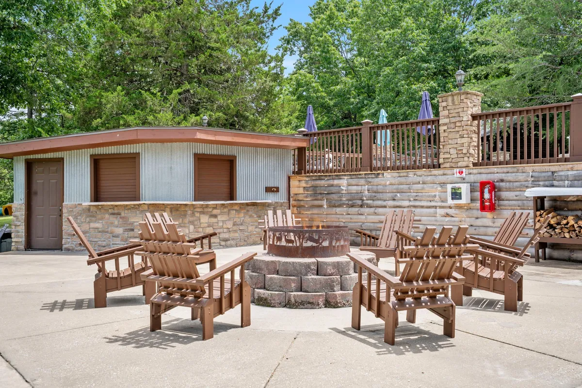 A cozy outdoor fire pit area with Adirondack chairs circling the fire, all set within lush greenery and adjacent to an outdoor deck. The scene suggests gathering, storytelling, and unwinding under the evening sky.