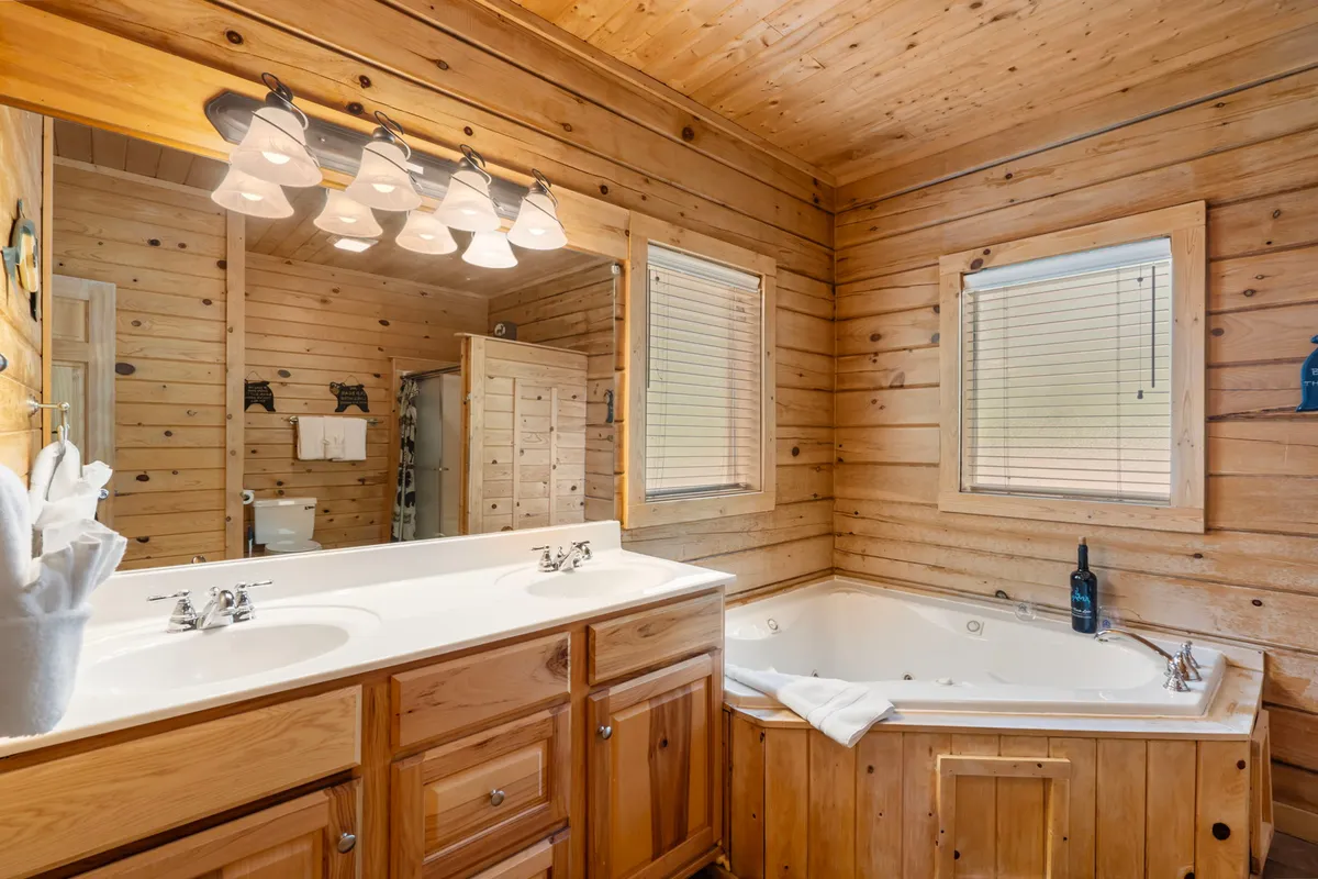 A luxurious bathroom featuring a double sink vanity, jacuzzi tub, wooden accents, and a mirrored wall. The space feels both upscale and inviting, ideal for unwinding after a long day.