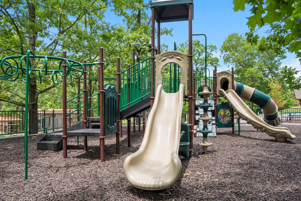 An inviting exterior shot of the resort’s playground featuring slides, a climbing structure, and swings, with children playing and families enjoying picnics under the trees.