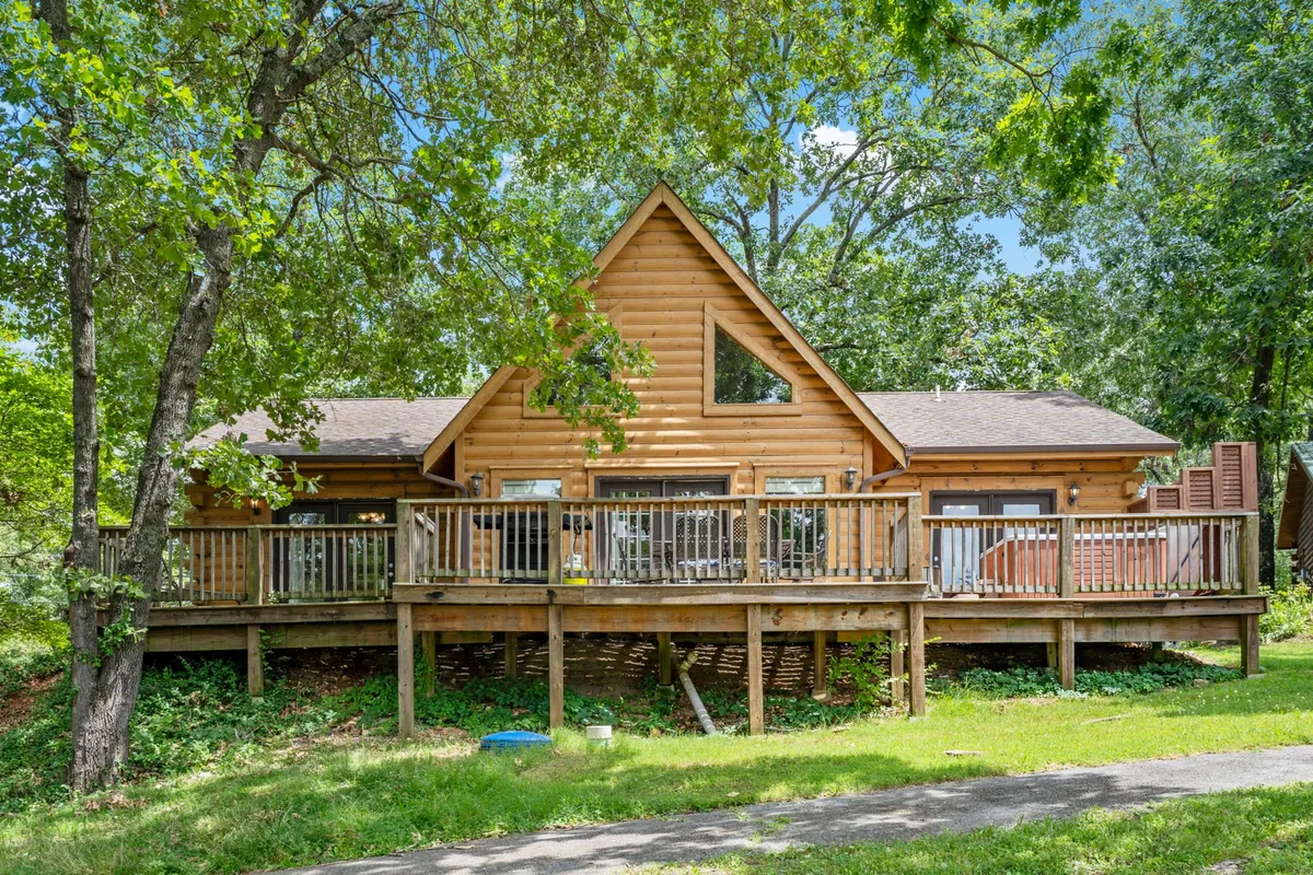 This image shows a welcoming wooden deck attached to the property, with large windows and an A-frame roof, set amongst trees. The deck is inviting, suggesting a space for socializing, relaxing, or enjoying a meal outdoors while immersed in nature.