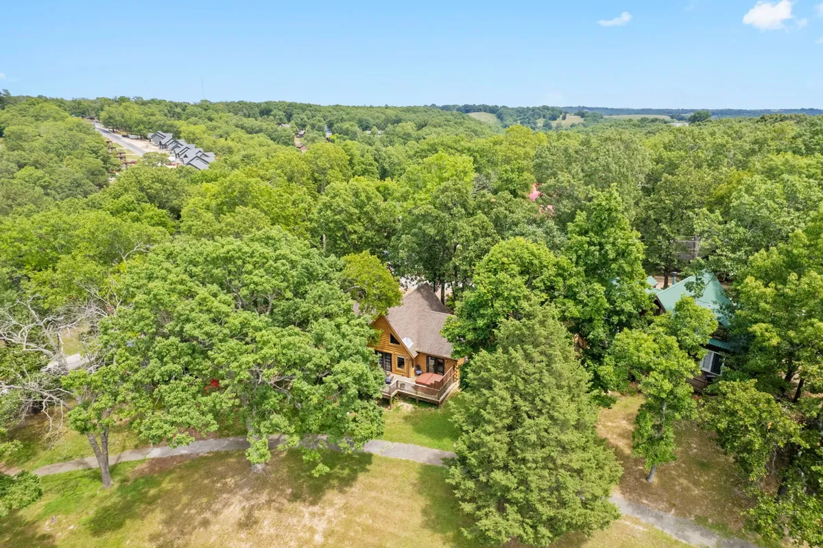 A charming log cabin is nestled among tall, leafy trees, with a winding pathway leading up to its welcoming front porch. The natural wood exterior and peaceful forested surroundings evoke a sense of privacy and tranquility—an ideal setting for couples looking to escape everyday life. The image hints at opportunities for relaxing outdoors and exploring the nearby woods.