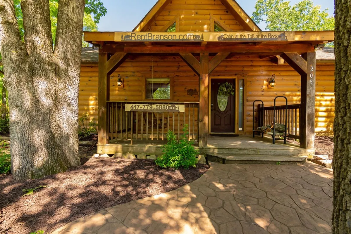 A classic log cabin with a spacious front porch sits among mature trees. The inviting porch is furnished for relaxation, providing a lovely vantage point for morning coffee or watching sunsets. The architecture and setting highlight the cabin's rustic charm and its close connection to the natural landscape.